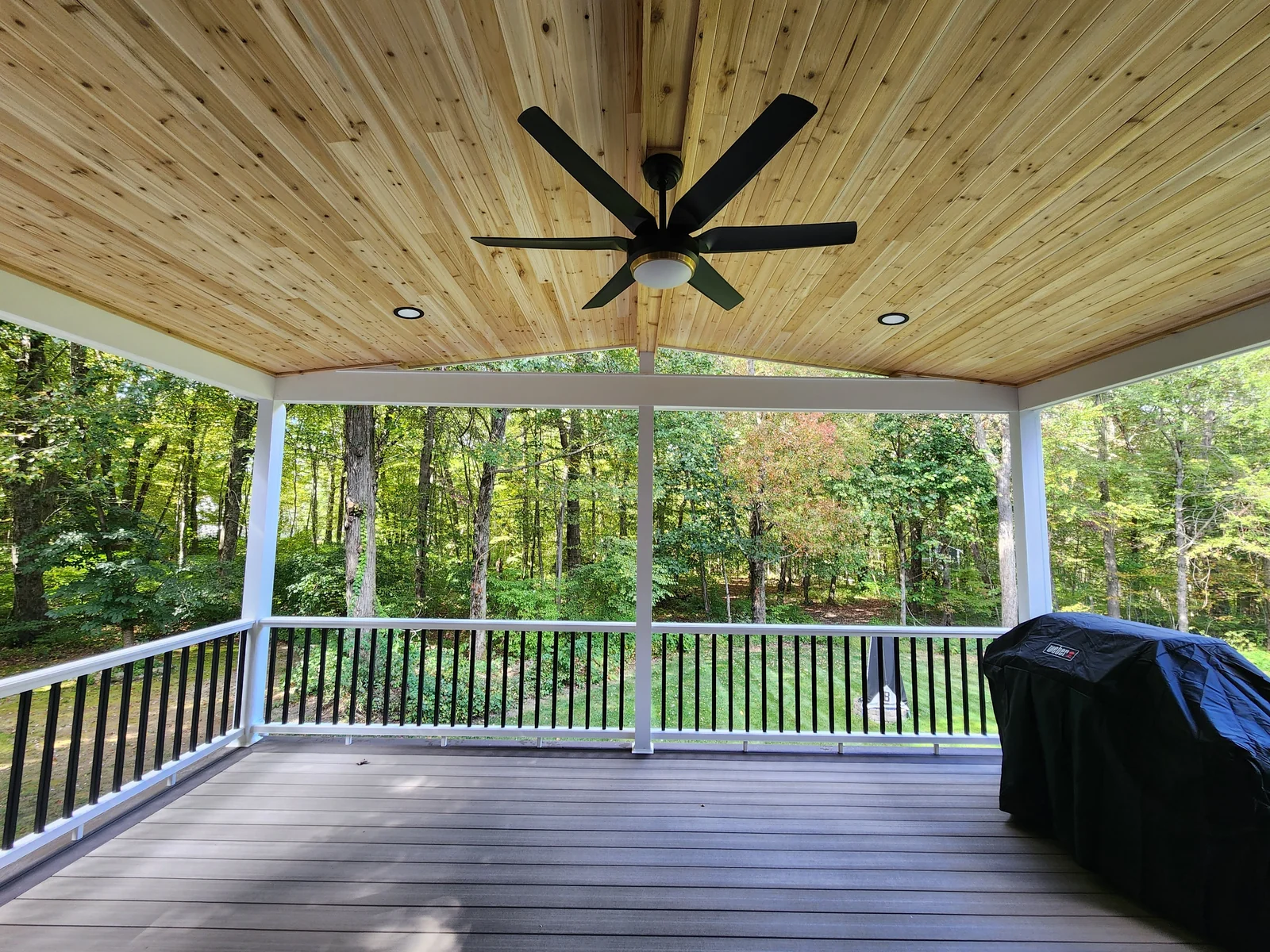 Covered deck with a wood ceiling, white framing, and a view of trees