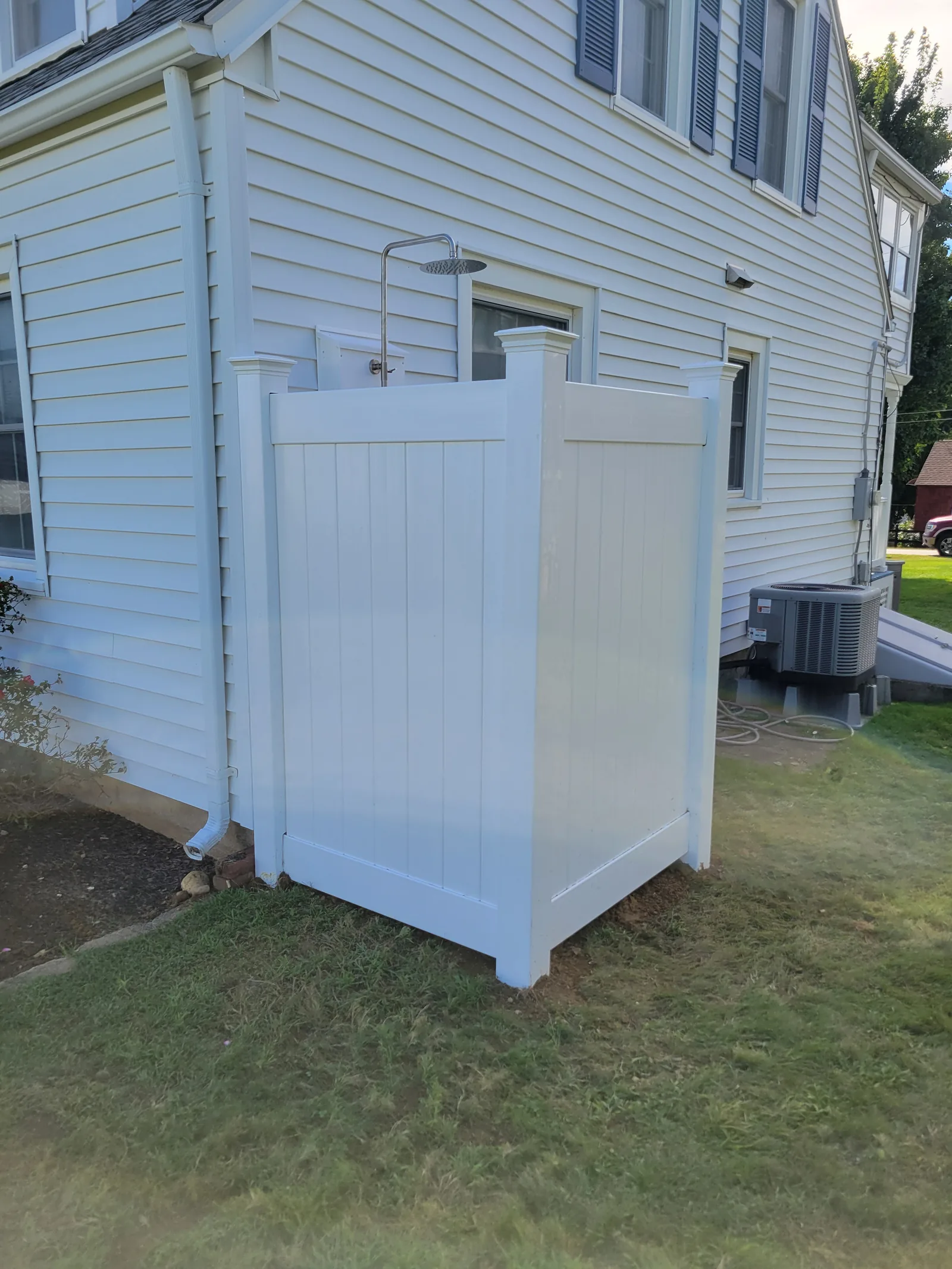 Finished outdoor shower enclosure with white vinyl panels at the corner of a white house